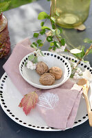Decorative table arrangement: plate and bowl with black polka dot rim, bowl filled with walnuts, DIY cloth napkin with leaf print