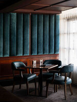 Dark wood table group with upholstered chairs in front of a blue velvet wall