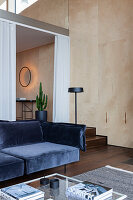Dark blue velvet sofa in modern living room with light-coloured wooden wall