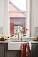 Flower-decorated kitchen sink with brass tap and view from the window