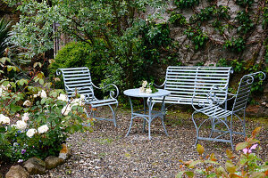 Seating area with metal furniture in a green courtyard in front of an overgrown wall