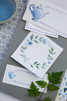 Hand-painted watercolour cards with blue flower and pitcher motifs on a grey background