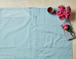 Taubenblaues Leinentuch, rosafarbene Rosen, Tasse Tee