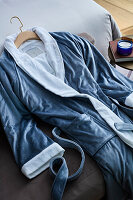 Blauer Bademantel mit weißem Kragen aus weichem Samt auf Bett liegend