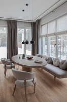 Helles Esszimmer mit ovalem Holztisch, grauem Polstersofa und schwarzen Hängeleuchten