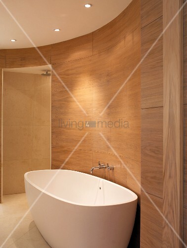 Freistehende Badewanne vor holzverkleideter Wand im ovalen, modernen ... Freistehende Badewanne vor holzverkleideter Wand im ovalen, modernen ...